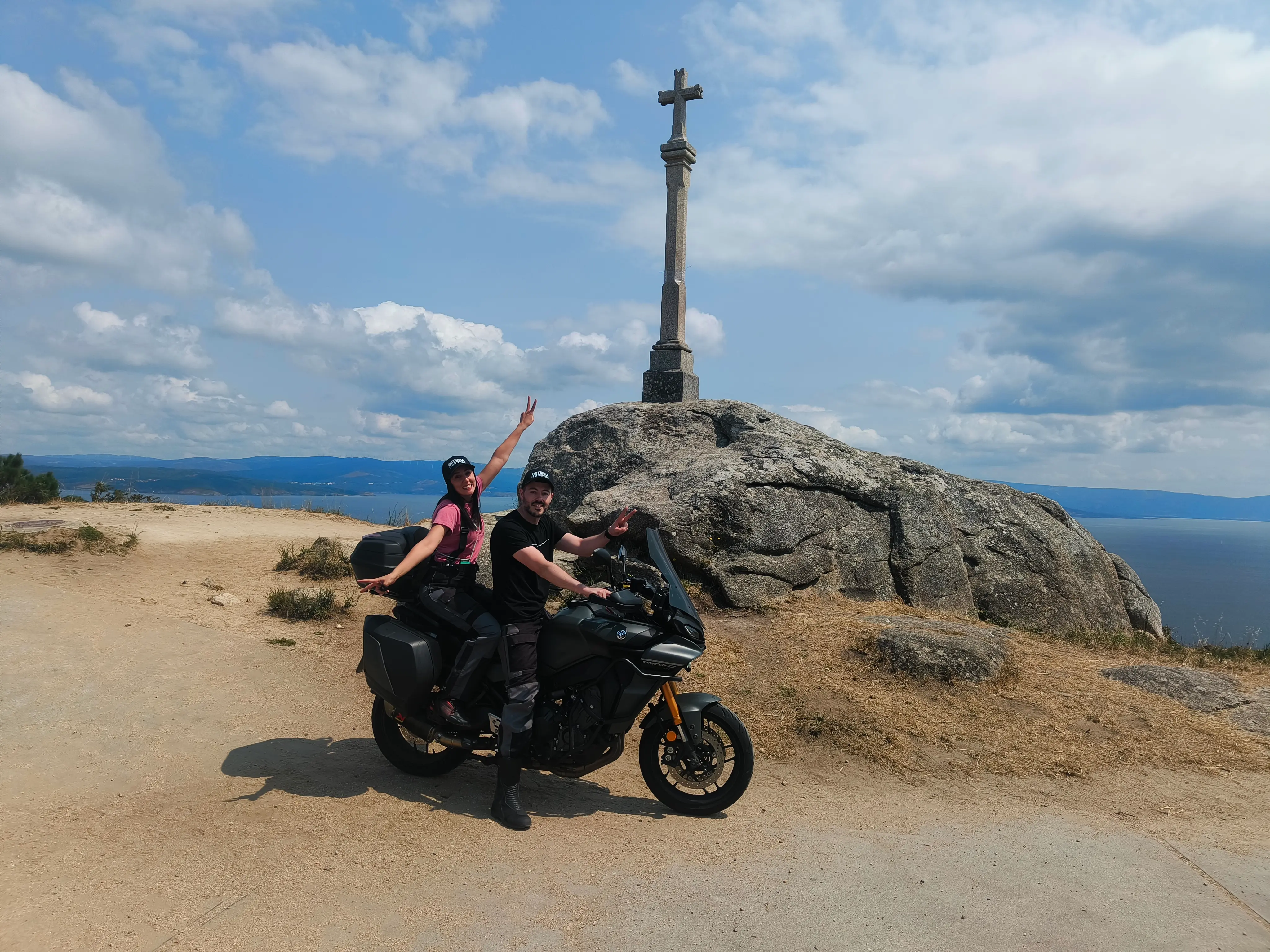Arantxa y Luis en una moto con un lago como fondo en el que aparece una cruz.